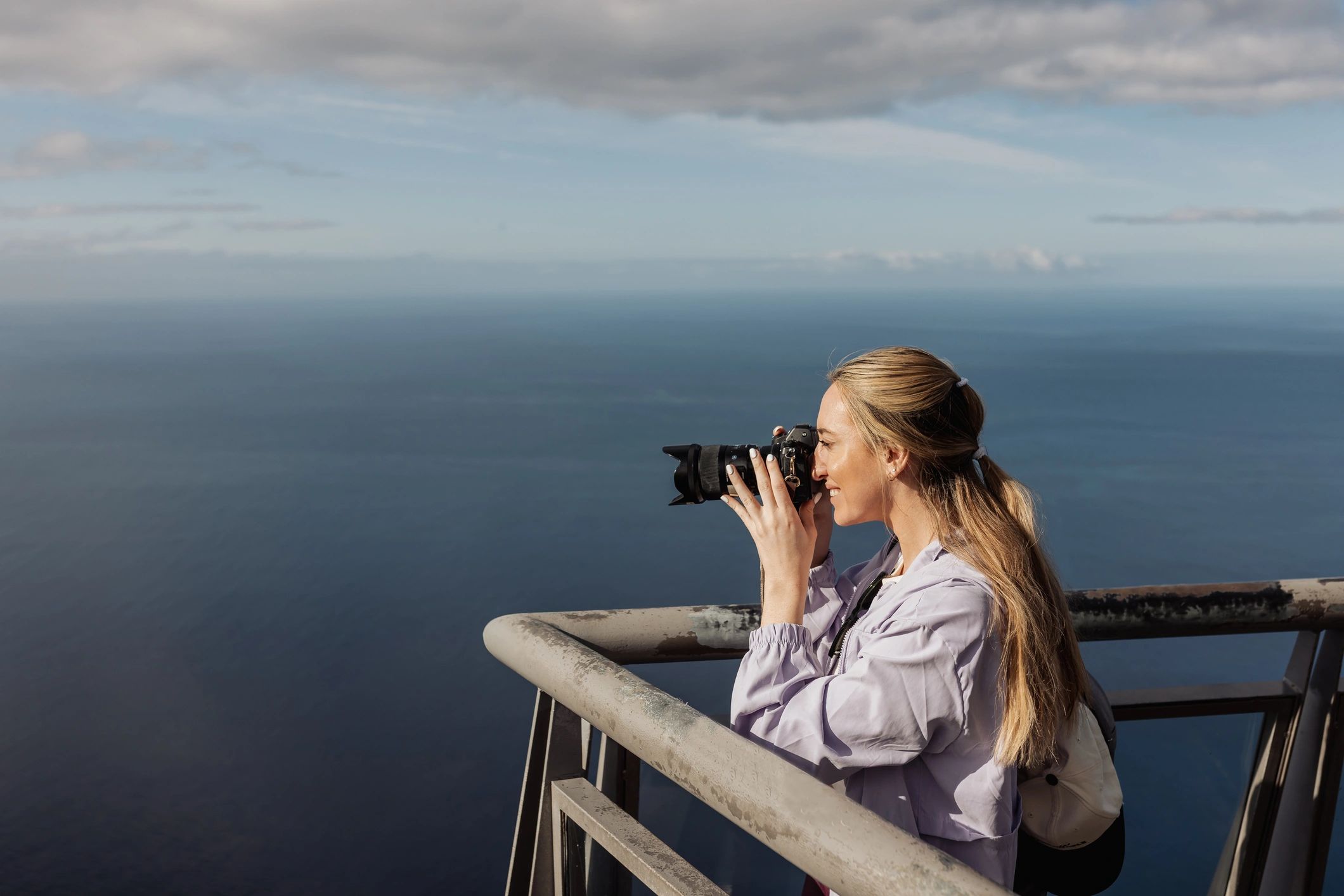 Young Woman Photographer Shooting Ocean View From Cliff Balcony in Madeira While Traveling